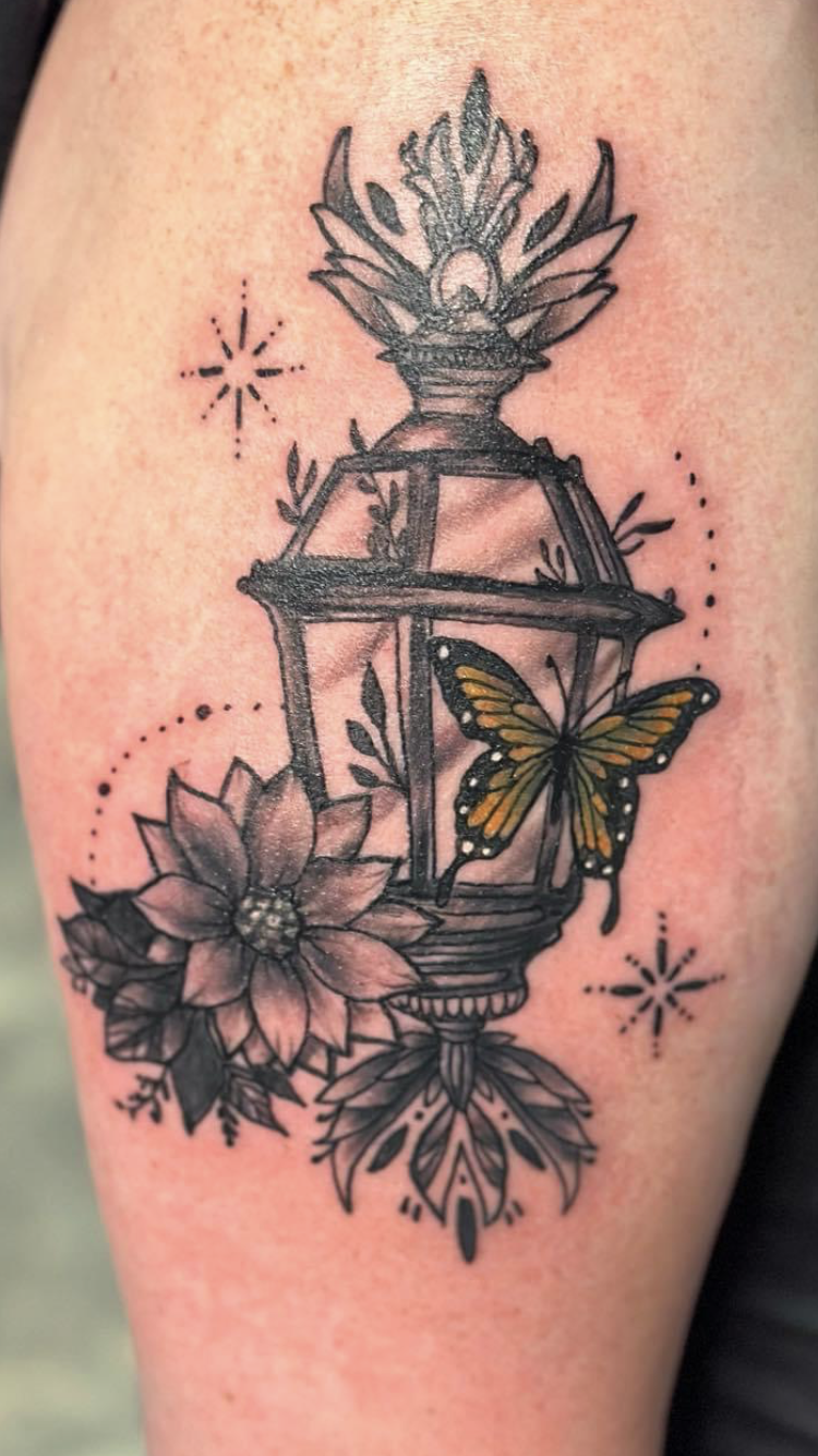Tattoo of a lantern with flowers and a butterfly on a client’s outer bicep